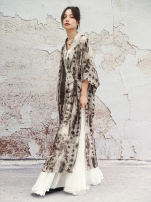 Modern Hanfu long cardigan in earthy geometric ink wash print with oversized bell sleeves and side split hem, styled over a flowing white maxi skirt outdoors