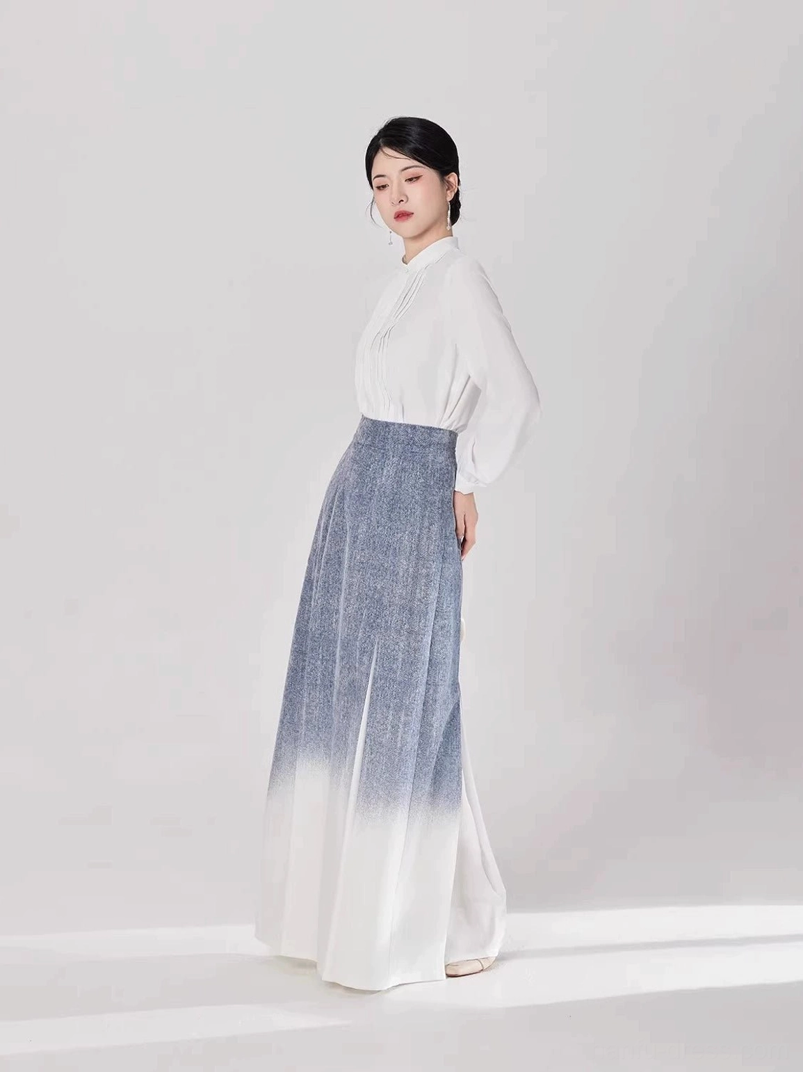 Side view of a woman wearing a modern Hanfu outfit with a flowing blue-to-ivory pleated gradient skirt