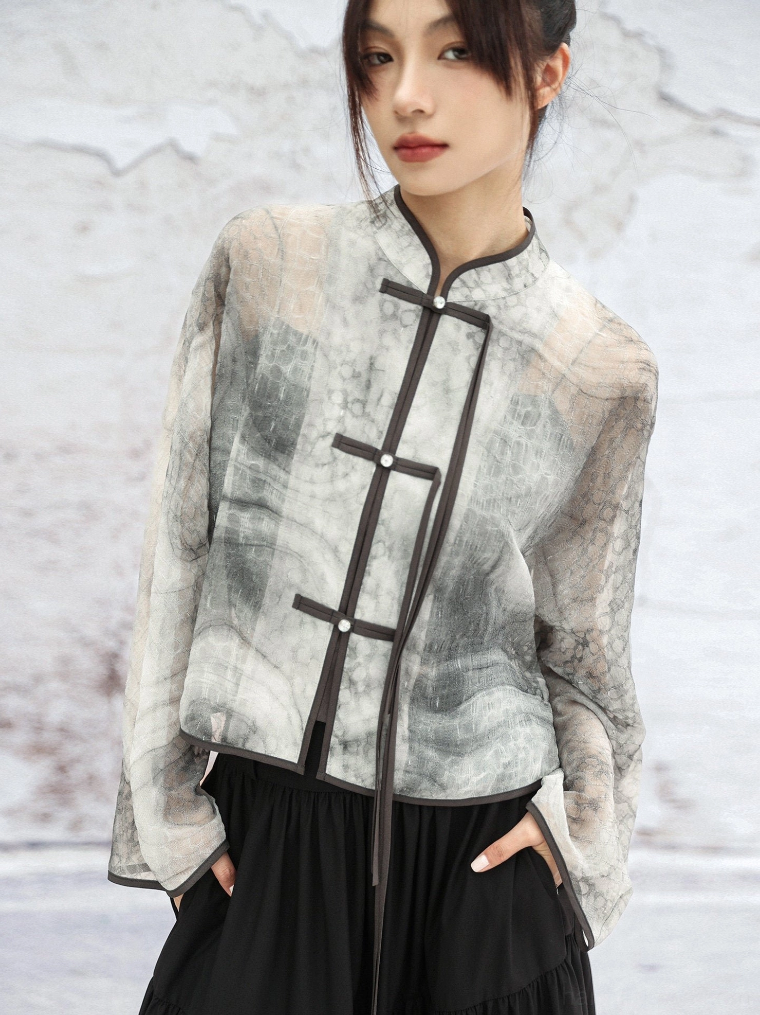 Close-up of modern Hanfu jacket featuring pearl-like frog buttons, dark piping, Mandarin collar, and marble ink-wash print