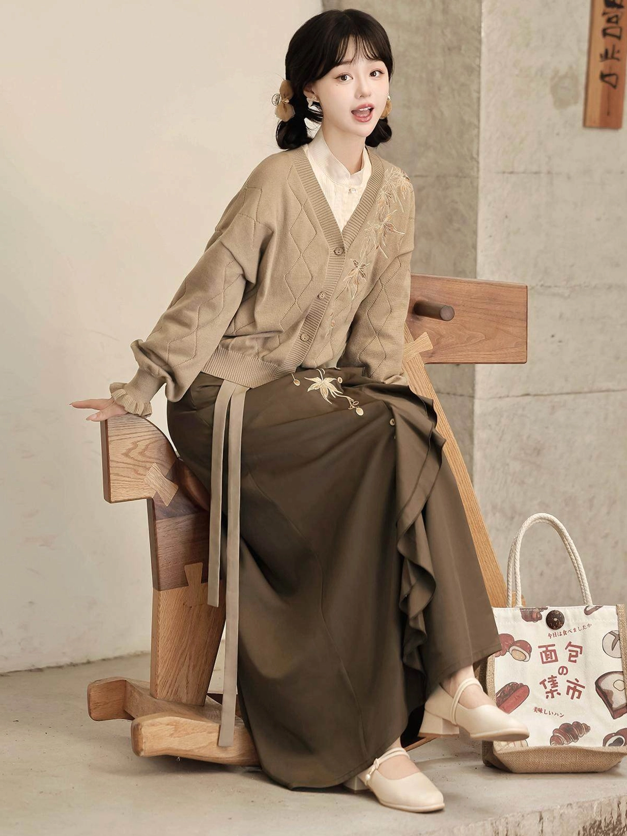 Full body seated view of a modern Hanfu knit cardigan and embroidered skirt outfit with waist sash decorative buttons and canvas tote