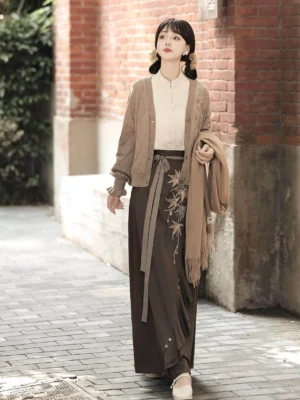 Full body view of a modern Hanfu knit cardigan and embroidered maple leaf skirt outfit styled on a vintage red brick street for an autumn date look