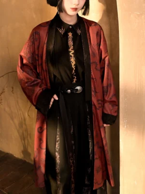 Close-up view of the modern Chinese style long coat showing the dark antique print, relaxed fit, black trim, gold embroidered inner shirt styling, and silver buckle belt