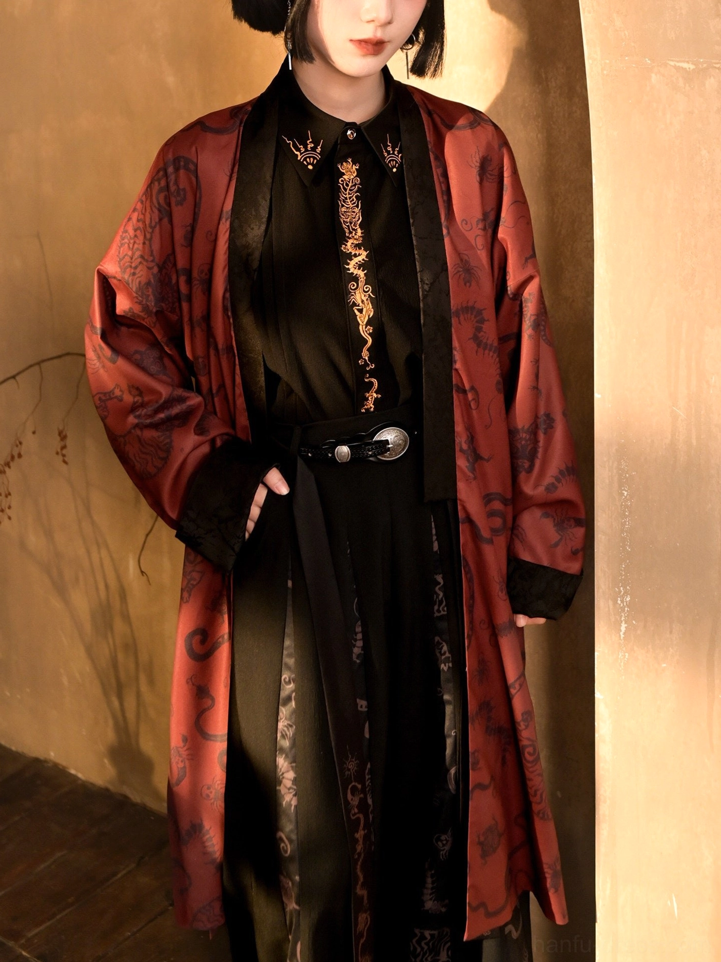 Close-up view of the modern Chinese style long coat showing the dark antique print, relaxed fit, black trim, gold embroidered inner shirt styling, and silver buckle belt