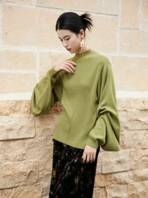Moss green modern Hanfu cashmere blend pipa sleeve knitted sweater shown from a left three-quarter angle with oversized lantern sleeves, stand collar, front seam, and dark printed midi skirt