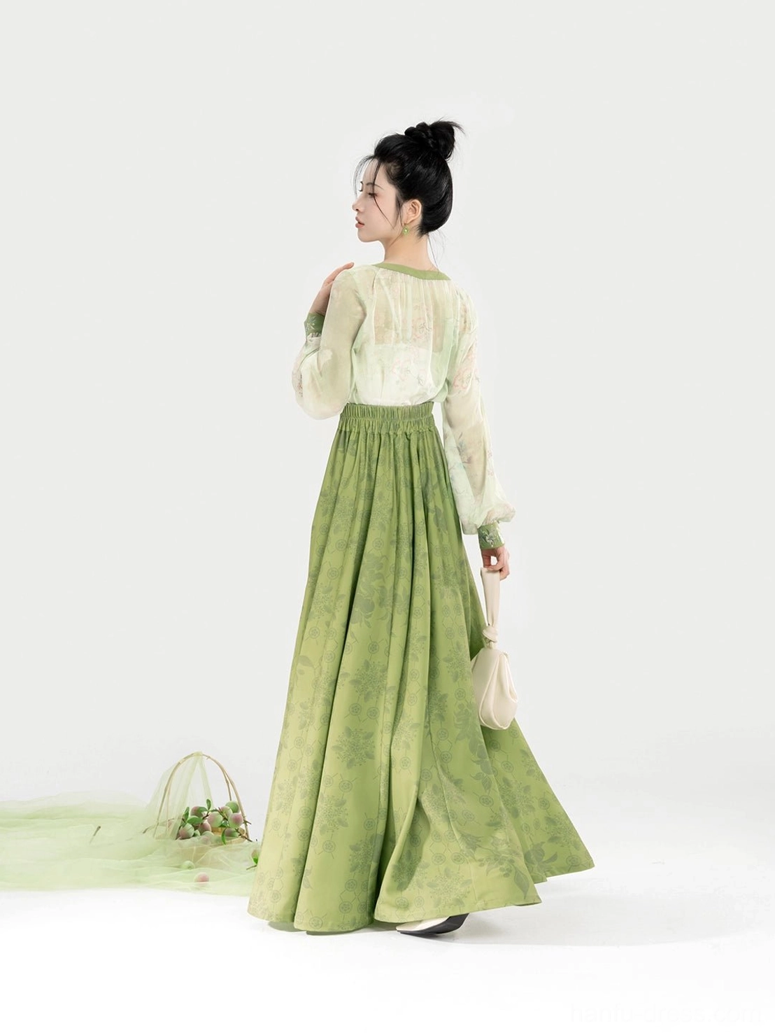 Back three-quarter view of a modern Hanfu outfit with sheer sleeves, embroidered waistband, and a full pleated sage green skirt with graceful drape