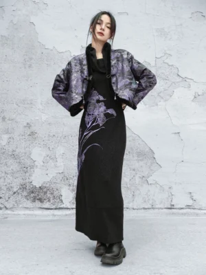 Full-body front view of a woman wearing a purple landscape jacquard modern Hanfu cropped jacket with black fuzzy trim styled over a black maxi dress with purple iris embroidery