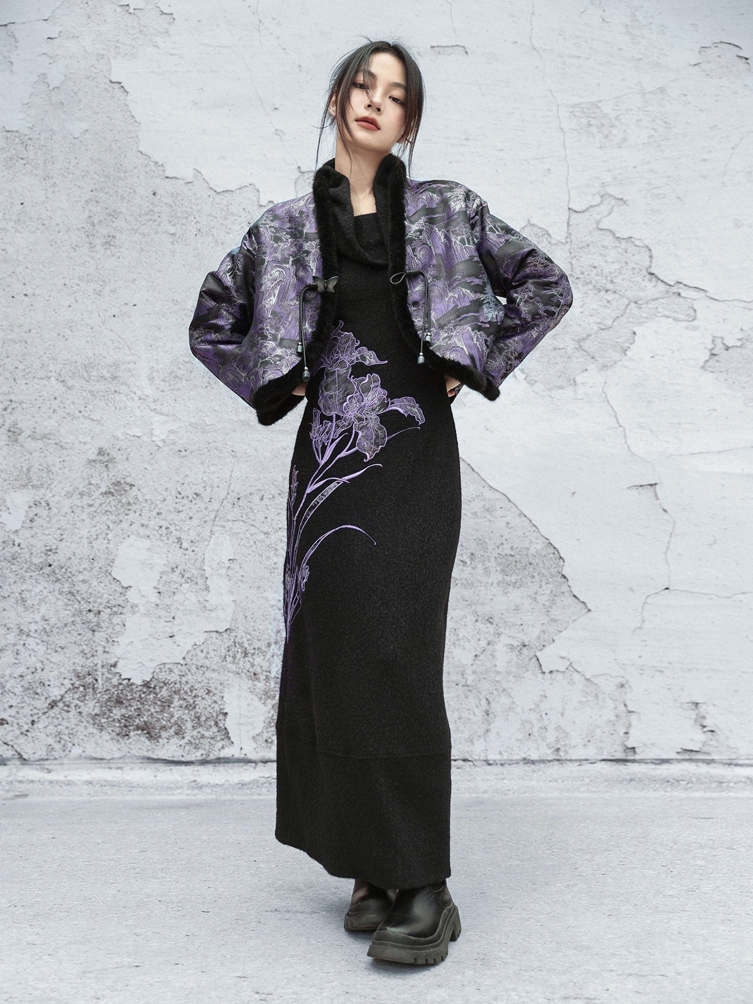 Full-body front view of a woman wearing a purple landscape jacquard modern Hanfu cropped jacket with black fuzzy trim styled over a black maxi dress with purple iris embroidery
