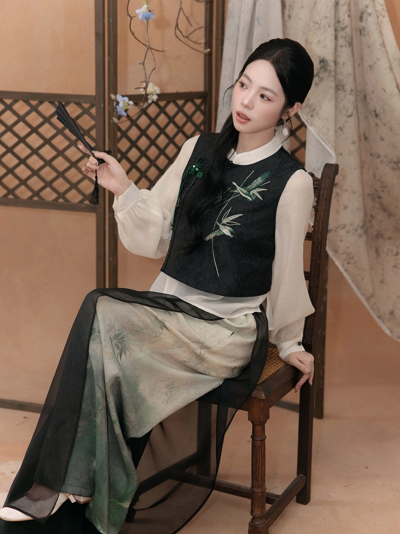 Seated view of a modern Hanfu clothing set showing the stand collar, Chinese knot buttons, bamboo leaf embroidery, and flowing wide leg pants