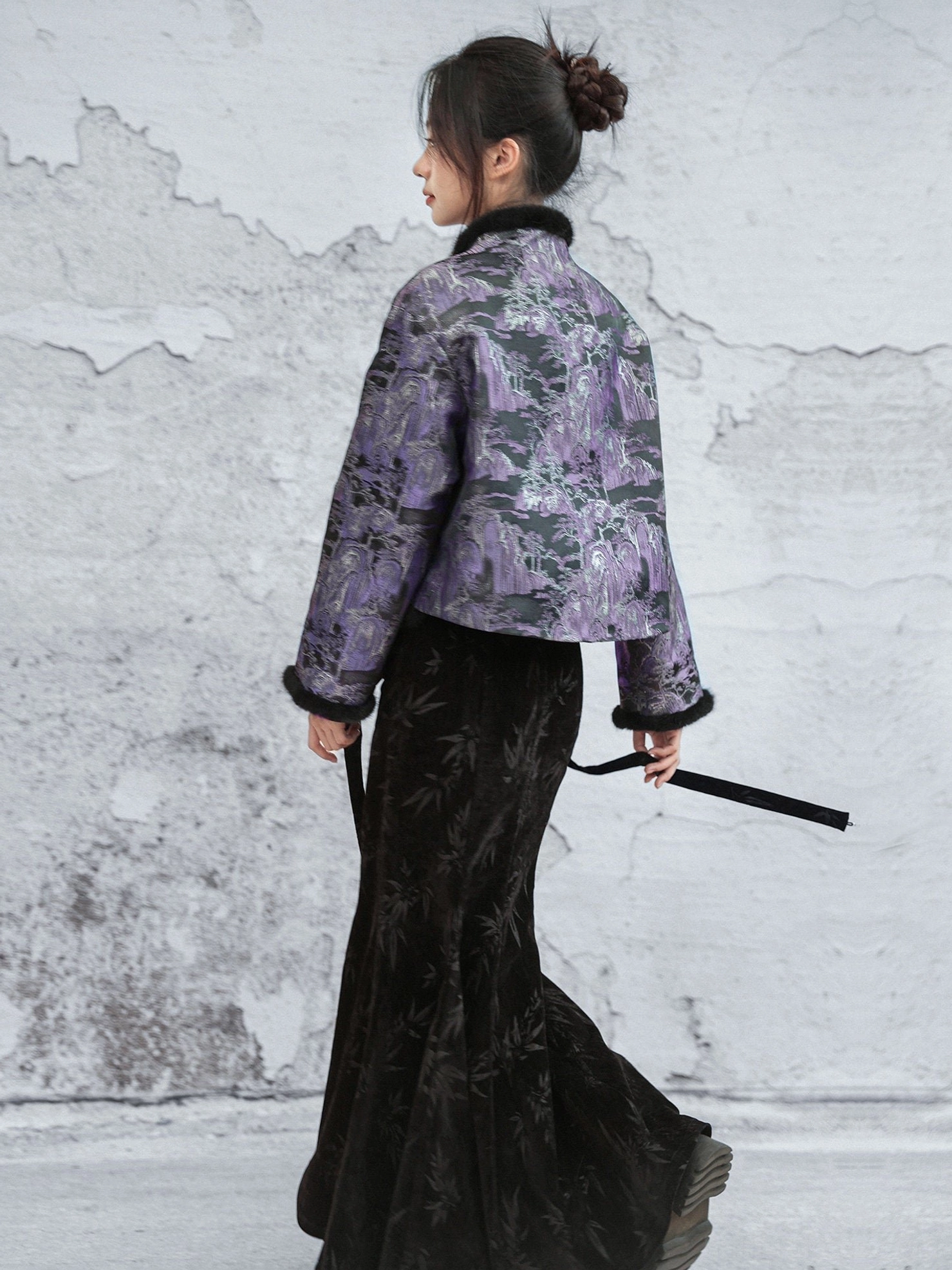 Back three-quarter view of a short modern Hanfu jacket showing the full purple landscape jacquard pattern black fuzzy collar and cuffs