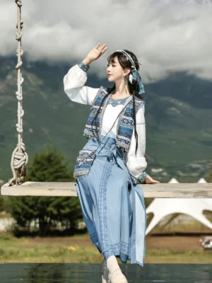 Sky blue modern Hanfu ethnic wrap skirt and embroidered vest outfit styled on a woman outdoors with a matching tassel crossbody bag
