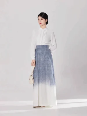 Front full-body view of a woman wearing a white stand-collar modern Hanfu top and blue-to-ivory gradient pleated maxi skirt