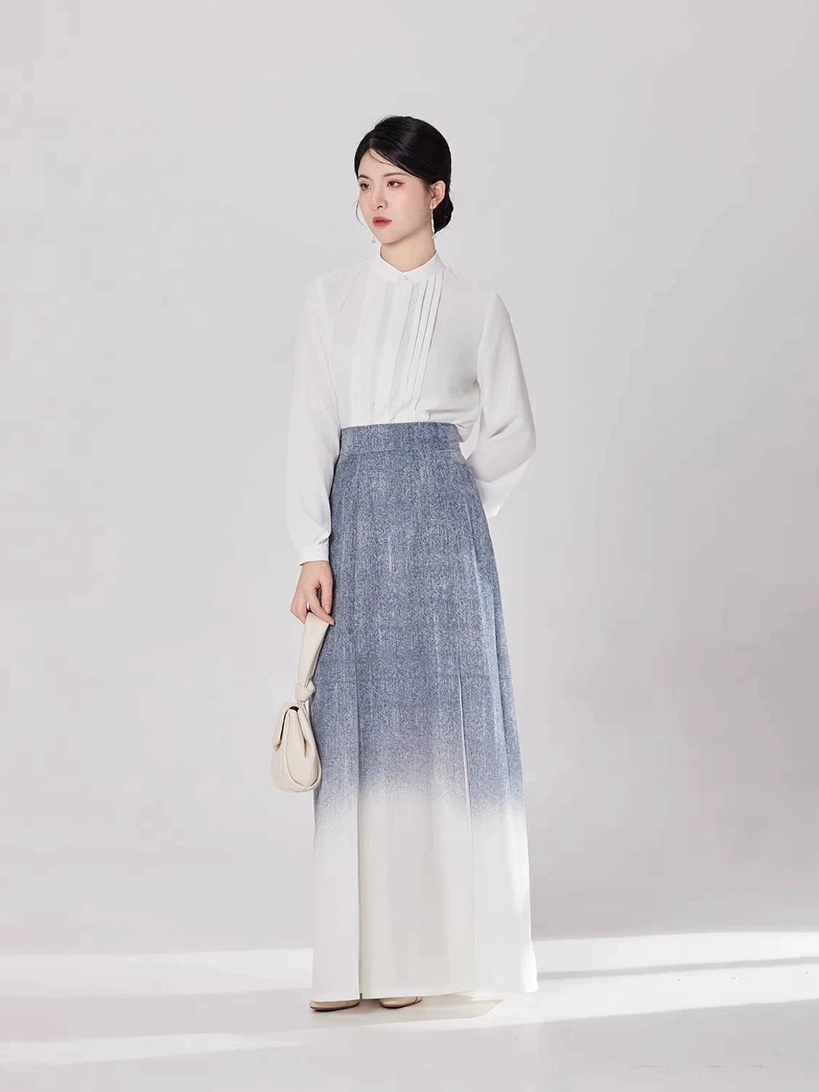 Front full-body view of a woman wearing a white stand-collar modern Hanfu top and blue-to-ivory gradient pleated maxi skirt