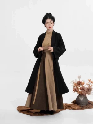 Full body view of a woman wearing a modern Hanfu three piece set with black long coat, khaki embroidered top, and two tone brown maxi skirt