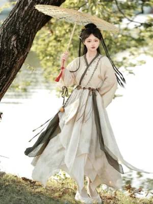 Modern hanfu xianxia little female apprentice costume with beige cross-collar top and asymmetrical olive green skirt styled beside a lakeside with a Chinese oil-paper umbrella