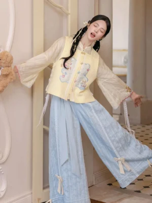 Modern Hanfu three-piece outfit with yellow embroidered vest, bell-sleeve top, and light blue bow-detail wide-leg pants styled on a model