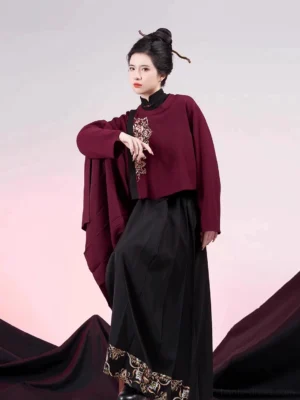 Three-quarter front view of a modern Ming Dynasty hanfu Jinxianghua outfit with dark red embroidered cropped jacket and black red pleated mamianqun-inspired culottes