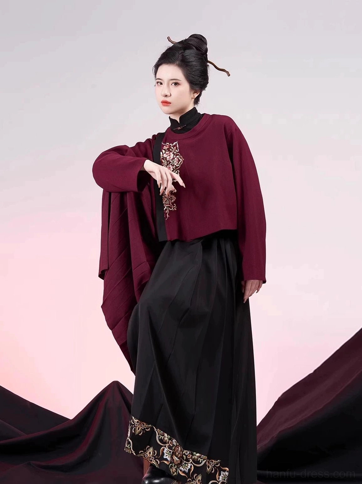 Three-quarter front view of a modern Ming Dynasty hanfu Jinxianghua outfit with dark red embroidered cropped jacket and black red pleated mamianqun-inspired culottes