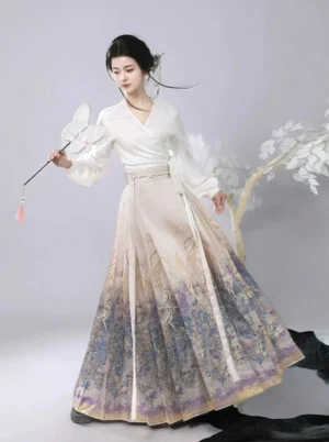 Modern Ming Dynasty hanfu mamianqun horse face skirt outfit with cream beige to purple blue ombre color, gilded butterfly floral and Chinese calligraphy print, shown on a model in an oriental studio