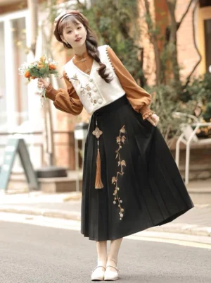 Full front view of modern Ming-inspired mamianqun Hanfu three-piece set with caramel lantern-sleeve blouse, ivory embroidered vest, and black horse face skirt