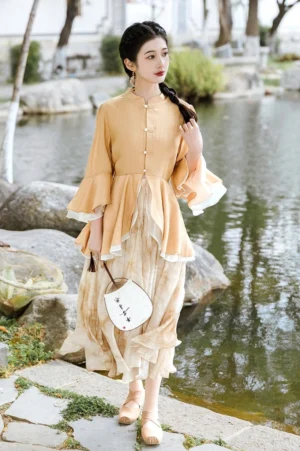 Full body modern Hanfu outfit featuring an apricot yellow Chinese stand collar top, flowing tie dye beige midi skirt, round Chinese fan, and beige flats