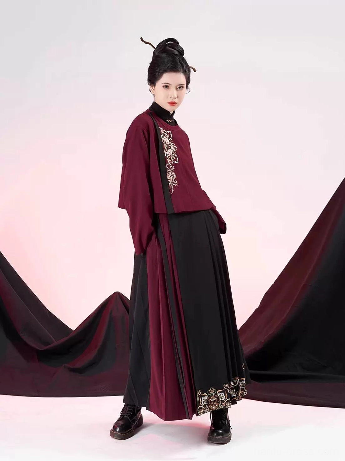 Side view of modern Ming-style hanfu clothing showing the dark red jacket, black contrast trim, red pleated panel, wrap drape, and embroidered culotte hem