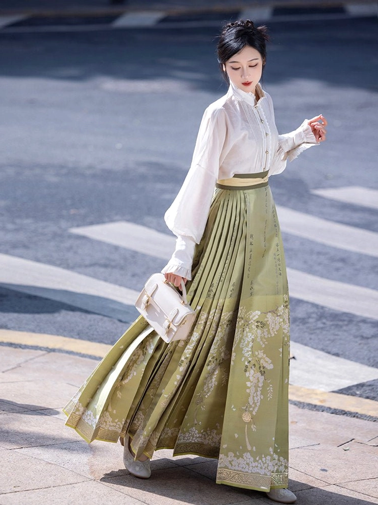 Modern Ming-style Hanfu outfit shown from a three-quarter angle with flowing sage green pleated mamianqun skirt and white lantern sleeve top