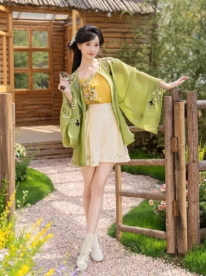 Modern Ming style Hanfu summer three piece outfit with green embroidered cardigan yellow camisole and beige shorts shown in a full body outdoor garden courtyard view