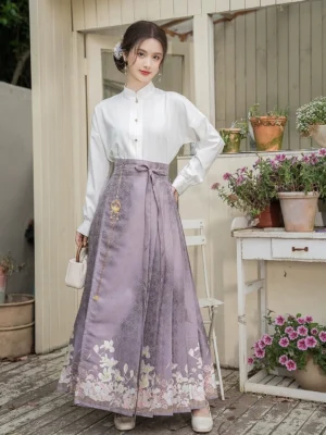 Front three-quarter view of a modern Ming-style Hanfu outfit featuring a white cross-collar blouse, tied waist sash, dusty purple mamianqun skirt, golden waist detail, and floral hem decoration