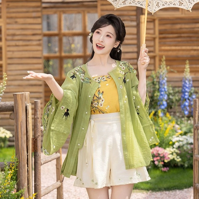 Modern Ming style Hanfu summer outfit with embroidered wide leg beige shorts and paper parasol in a bright outdoor flower garden