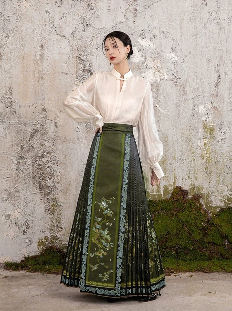 Front three-quarter view of a dark olive green modern Ming style mamian skirt with pleats, floral decoration, light blue trim, and high waist Hanfu design