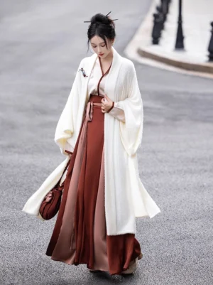 Modern Song Dynasty Hanfu full outfit worn by a woman outdoors, featuring an ivory fuzzy beizi-style jacket, light pink embroidered cross-collar blouse, burgundy two-tone wrap skirt, and matching handbag