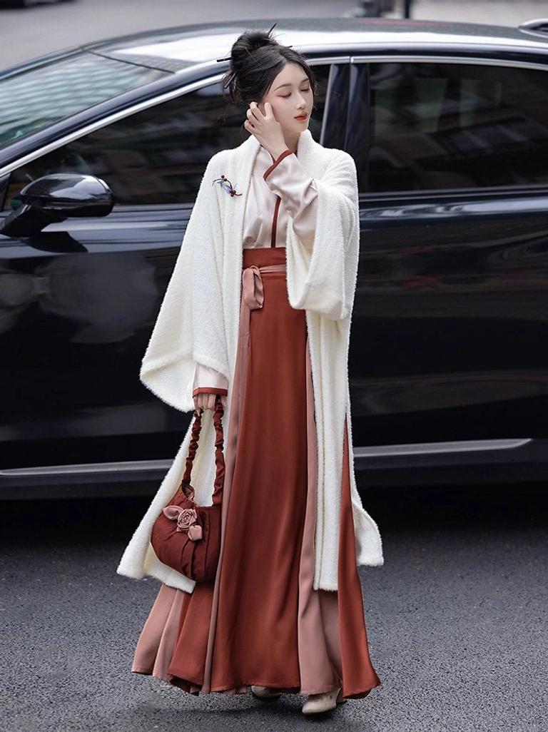 Side view of a modern Song Dynasty Hanfu outfit with ivory long jacket, floral lapel brooch, burgundy satin wrap skirt, contrast cuffs, and matching Chinese-style handbag