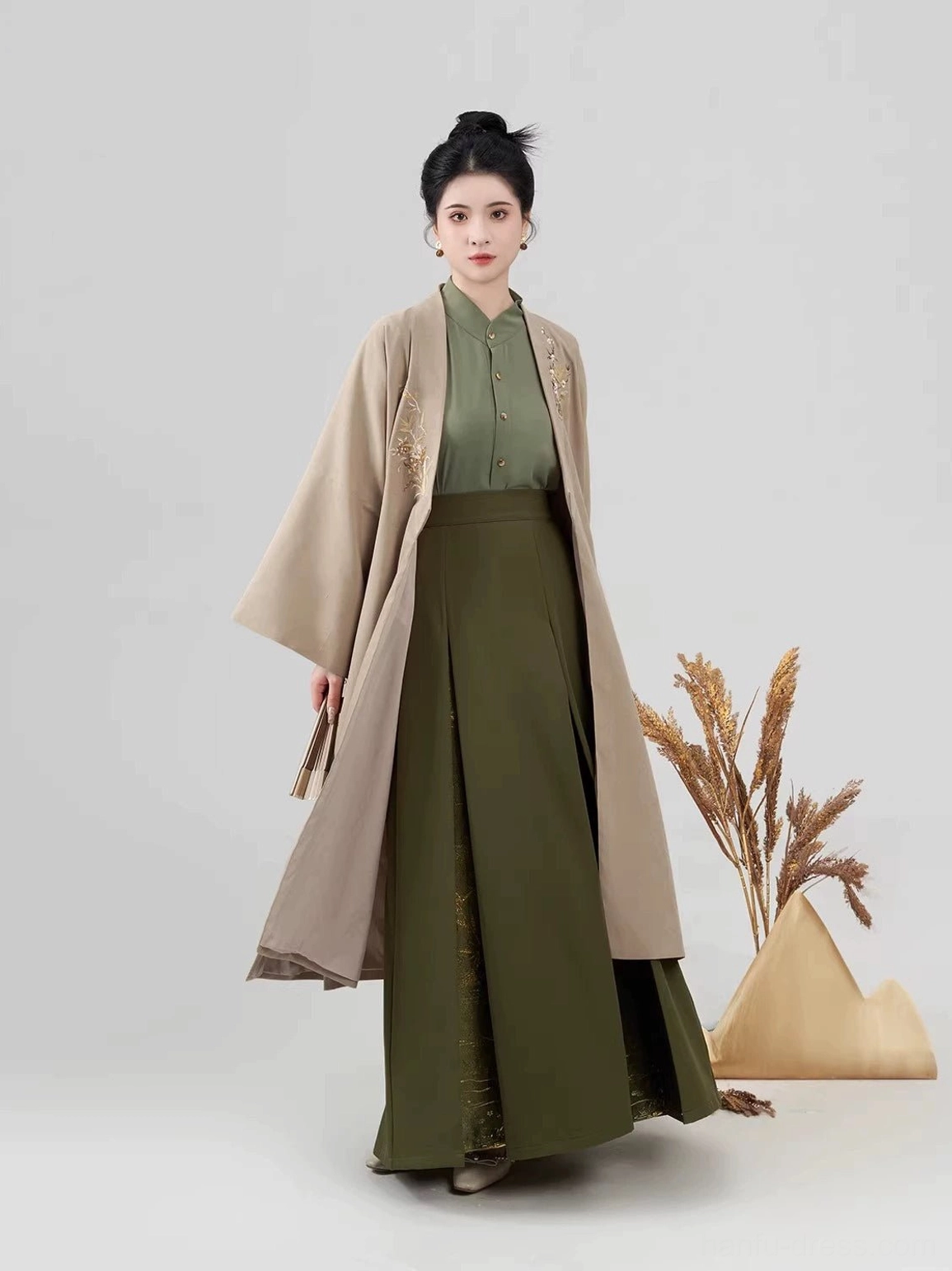 Three-quarter view of a woman modeling a modern Song Dynasty Hanfu outfit with a loose light khaki outer coat and flowing green pleated skirt