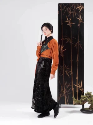 Modern Song Dynasty Hanfu set with burnt orange long sleeve jacquard top, black wrap skirt, and traditional Chinese-inspired styling in a bamboo studio