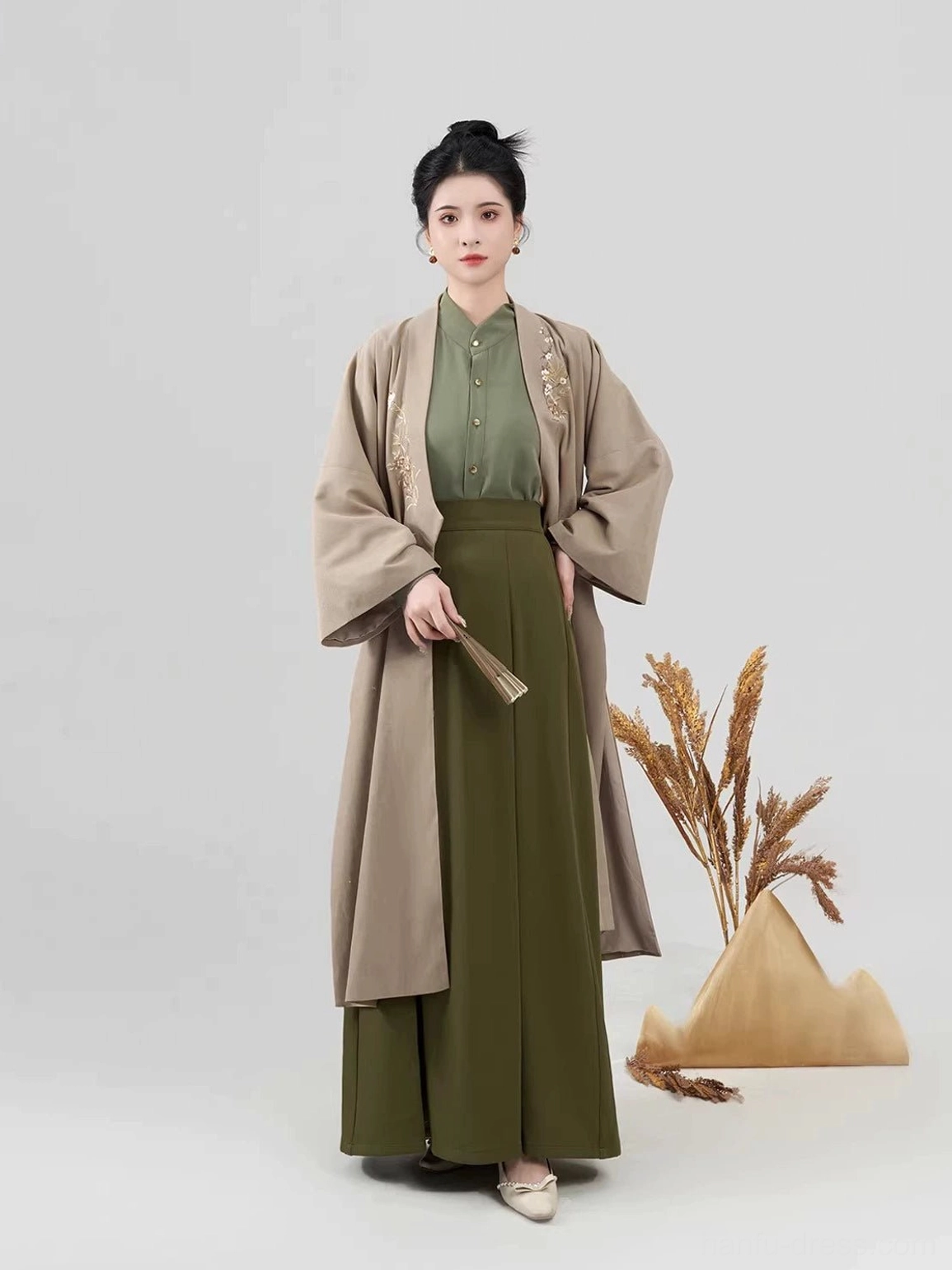 Full-body front view of a woman wearing a three-piece modern Song Dynasty Hanfu set with a light khaki embroidered coat, army green long-sleeve top, and pleated skirt