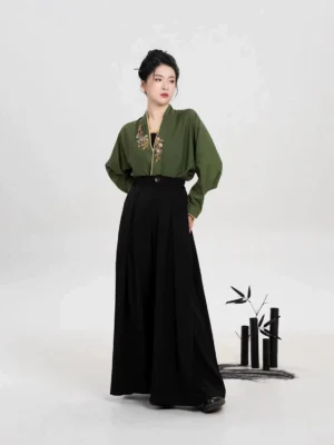 Modern Song Dynasty Hanfu set with olive green embroidered winged sleeve top and black wide leg pants worn by a model in a bamboo inspired studio