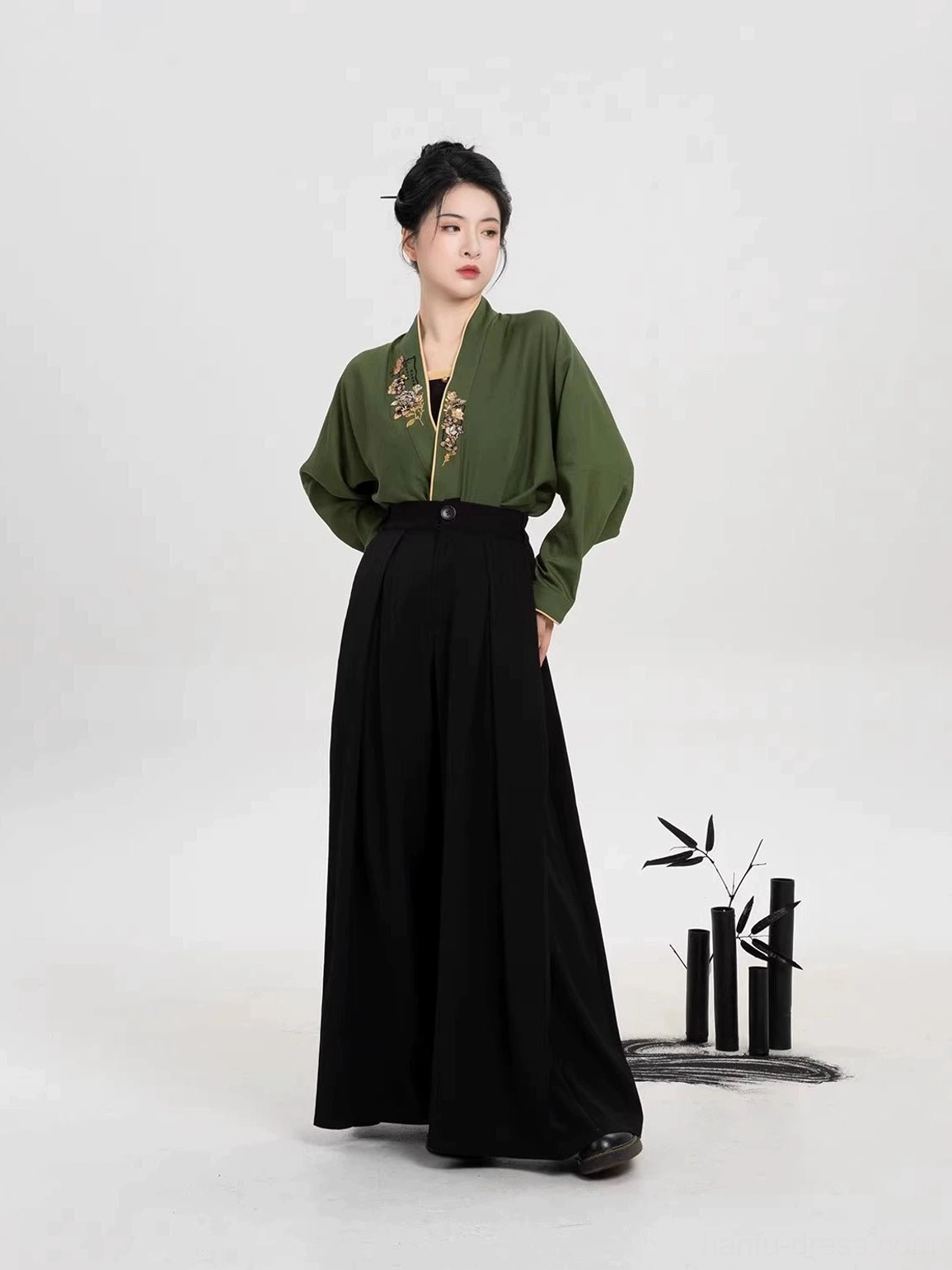 Modern Song Dynasty Hanfu set with olive green embroidered winged sleeve top and black wide leg pants worn by a model in a bamboo inspired studio