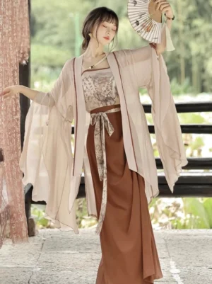 Modern Song Dynasty Hanfu three-piece outfit with apricot sheer wide-sleeve coat, printed camisole and caramel skirt by a lakeside pavilion