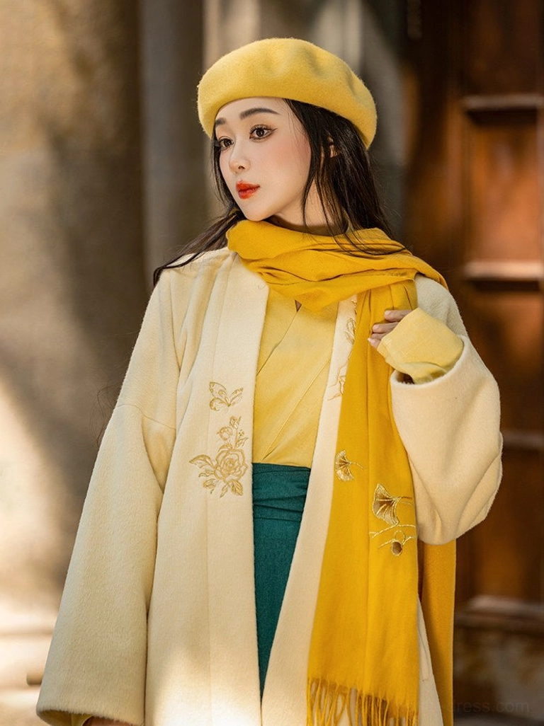Close-up of modern Song Hanfu styling showing delicate floral embroidery on a cream wool blend jacket with mustard inner top and beret