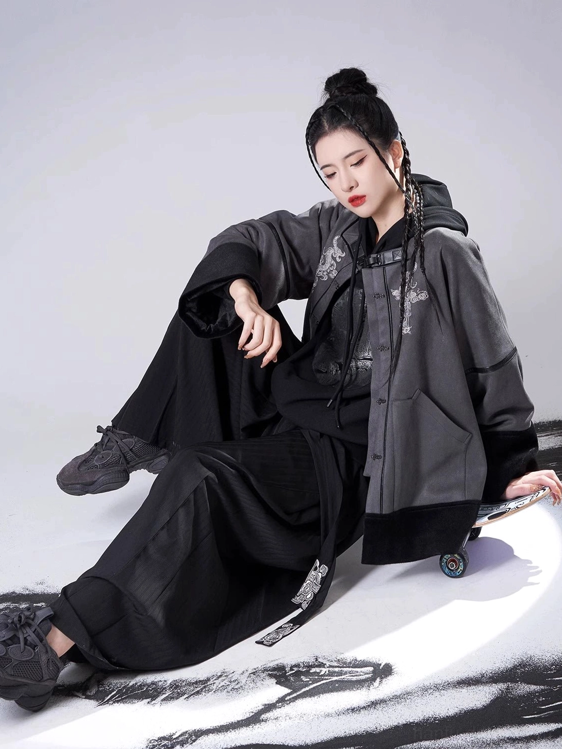 Seated side view of a contemporary Song Dynasty Hanfu outfit with an unbuttoned jacket, black hooded sweater, wide-leg pants, and tassel waistband detail