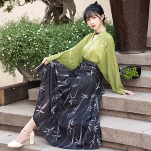 Modern Song-inspired Hanfu outfit with pistachio green wide-sleeve top yellow camisole and flowing bamboo-print skirt shown in a garden sitting pose