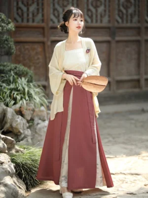 Modern Song-style Hanfu three-piece outfit with relaxed cardigan, layered printed skirt, square-neck camisole, and wooden hand fan in a traditional Chinese garden