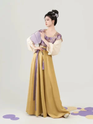 Three-quarter front view of purple and mustard Tang Dynasty hanfu with floral beizi, golden waist trim, long sashes, and traditional fan