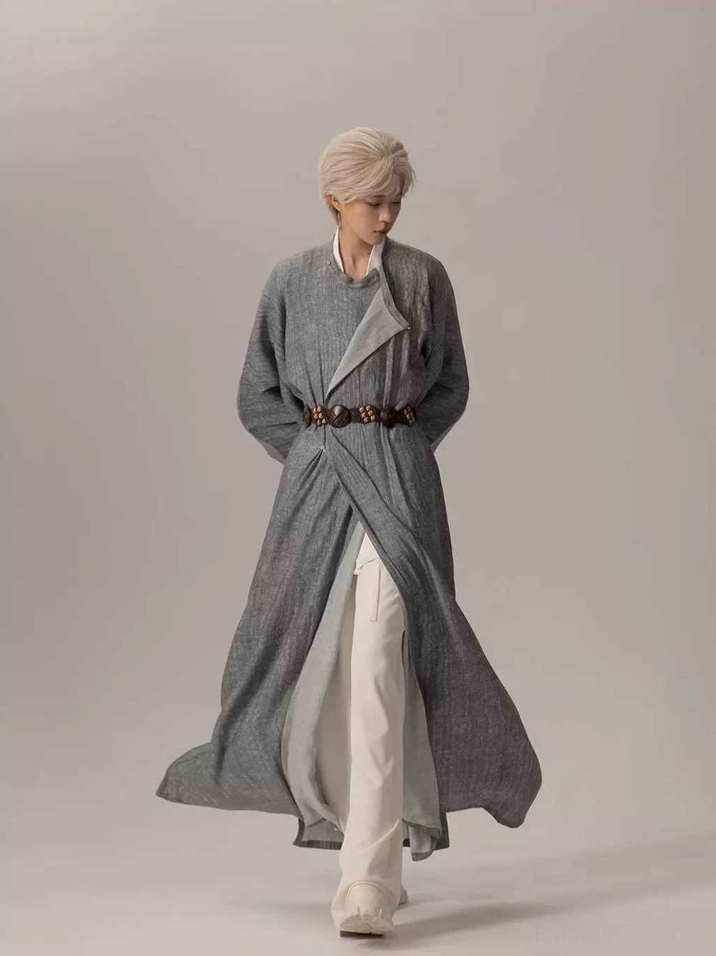 Front three quarter view of a modern Tang Dynasty Hanfu robe in heather grey with oversized sleeves, side split hem, cross-wrap front, and brown waist belt