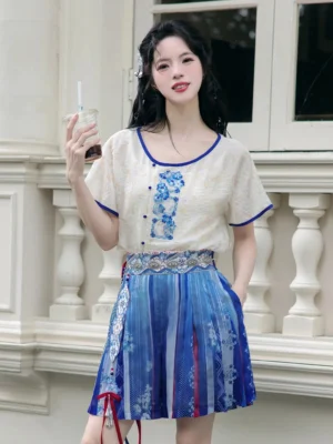 Modern Tang style Hanfu cropped embroidered top with blue pleated shorts skirt, silver waist chain, and red tassel details on a balcony