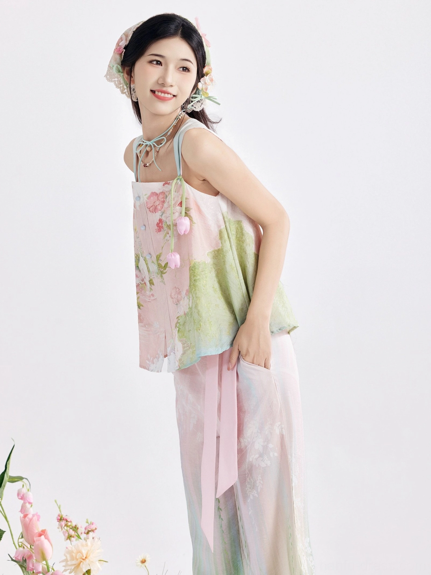 Close-up side view of a modern Tang-style Hanfu camisole with hanging tulip embellishments, long pink waist sash, pastel floral print, and matching headscarf