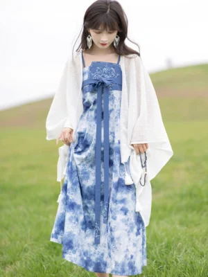 Front full-body view of a modern Tang style Hanfu dress with blue and white ripple tie dye, white shawl, tassel waist sash, and flowing midi skirt outdoors
