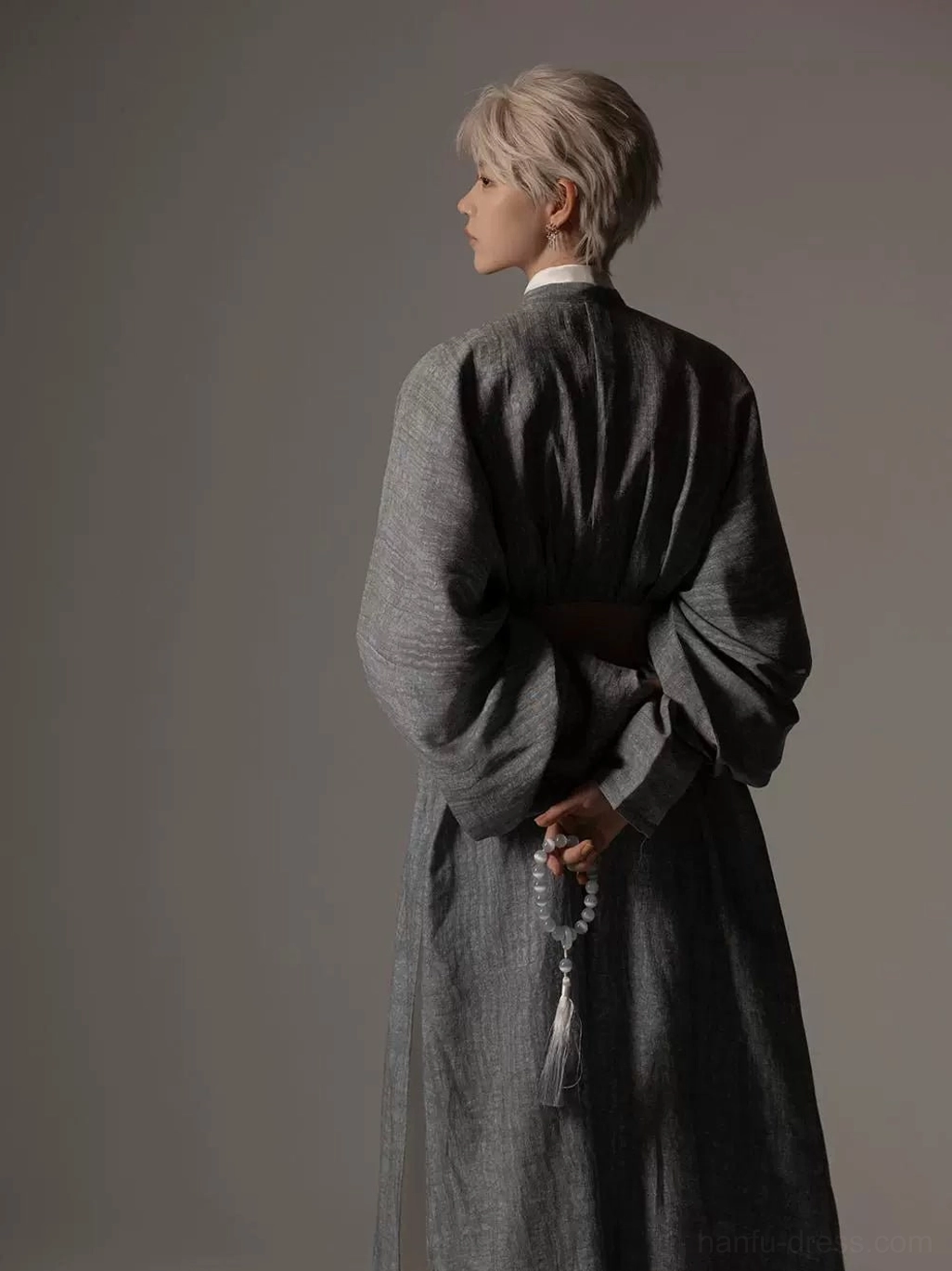Back view of a contemporary Tang style Hanfu robe showing the long loose silhouette, textured grey polyester fabric, closed back, wide sleeves, and waist belt