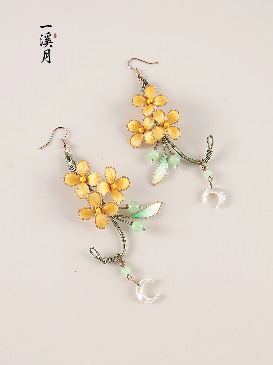 Detailed flat lay of moon laurel inspired Hanfu earrings with warm yellow osmanthus flowers leafy green accents and moon charms