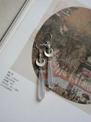 Moon Over Sea Chinese earrings photographed on a vintage Chinese painting page showing crescent moon pendants green beads and clear teardrop dangles